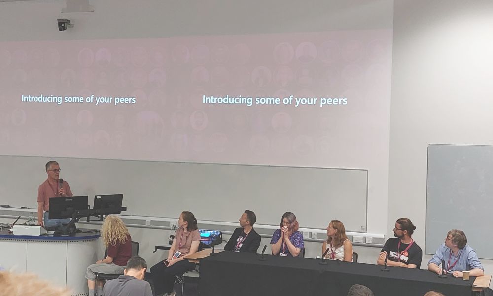 A man delivering a talk and a group of people sitting behind a table